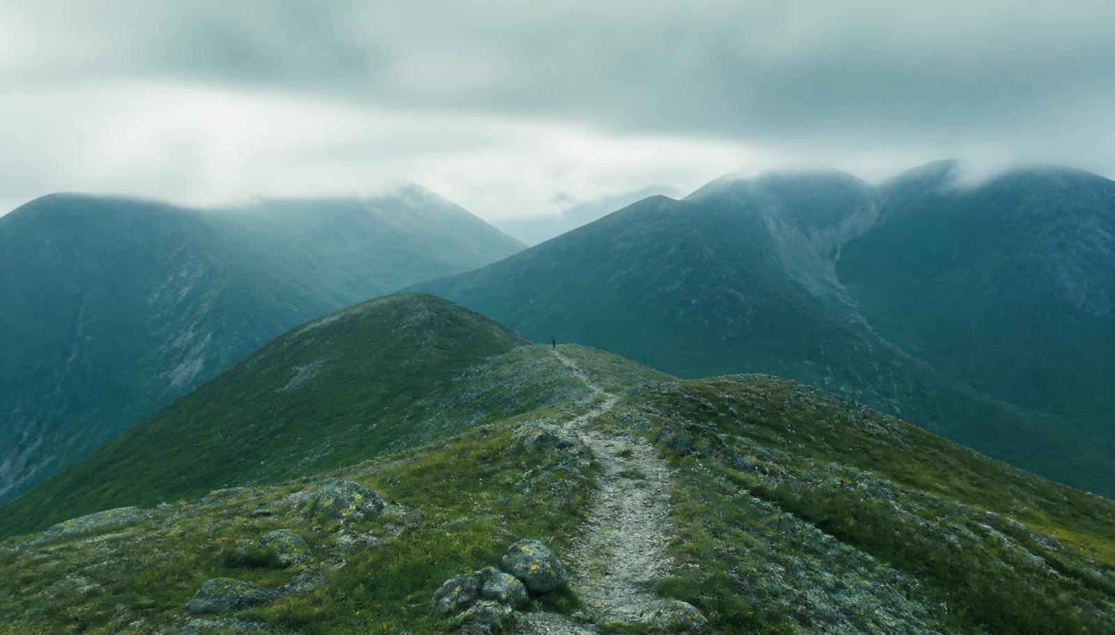 A hill path traversing a ridge in low cloud, the route ahead visible